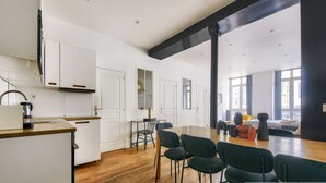 Una cucina moderna con mobili bianchi, un piano di lavoro in legno e un bollitore. C'è un'area pranzo con un tavolo in legno e sedie nere. La stanza ha ampie finestre e vista sulla città.