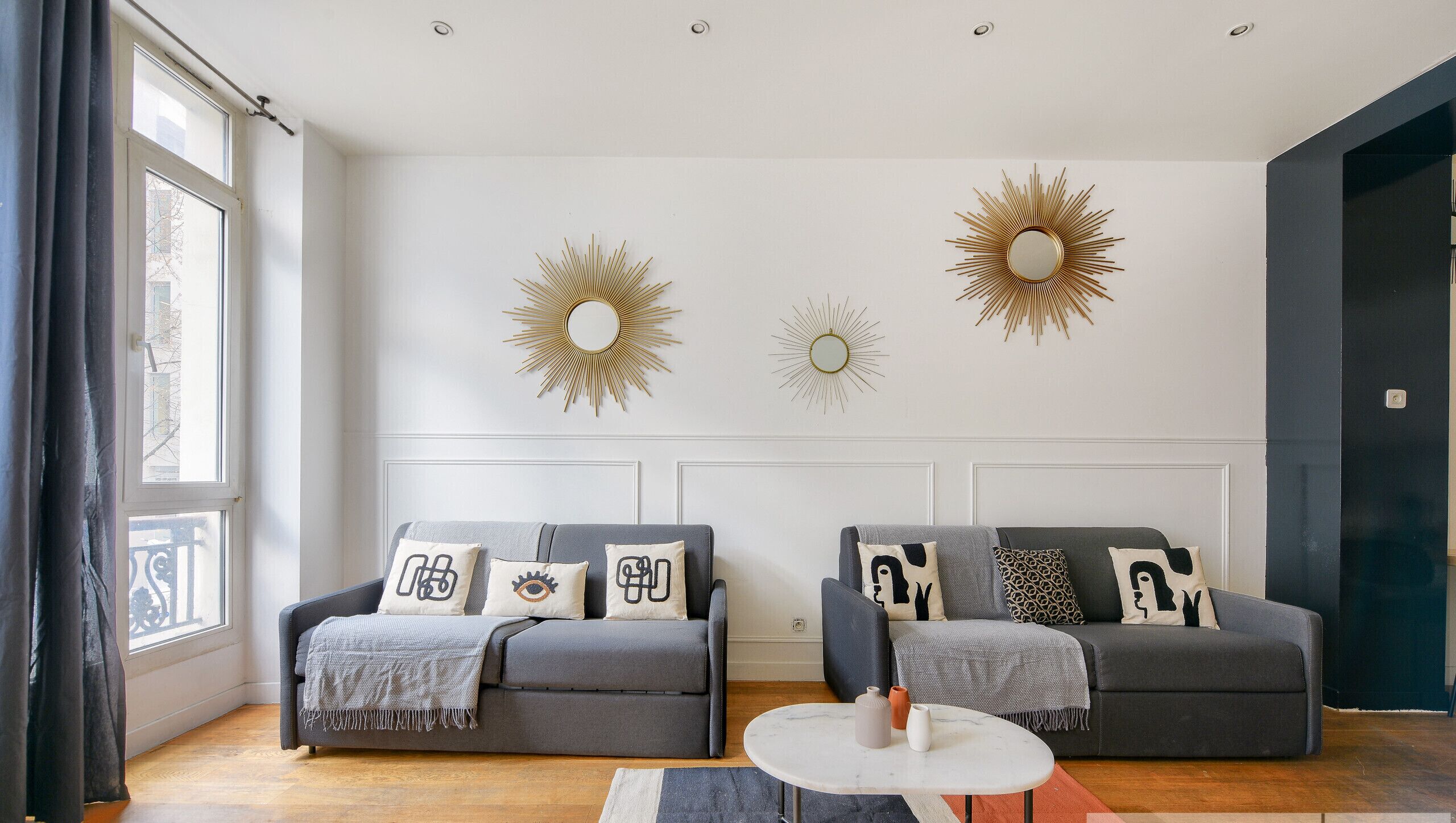A modern living room with two grey sofas, a round coffee table, and decorative sunburst wall art.