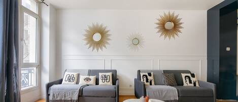 A modern living room with two grey sofas, a round coffee table, and decorative sunburst wall art.