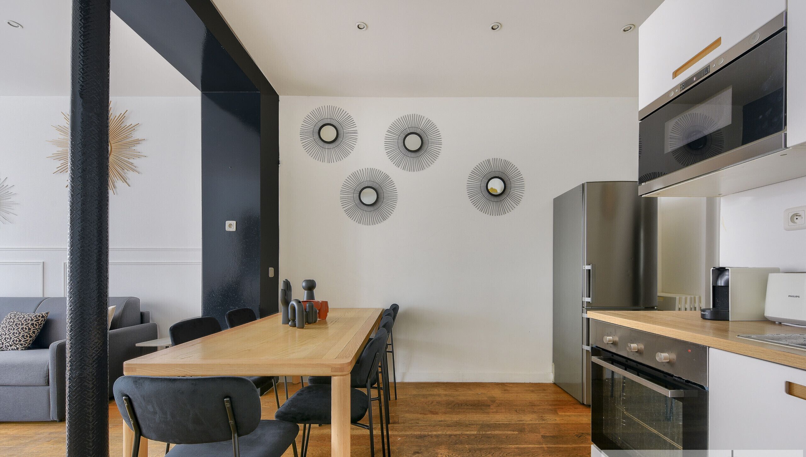Une cuisine moderne dotée d’un four encastré et d’un coin repas avec une table et des chaises en bois.