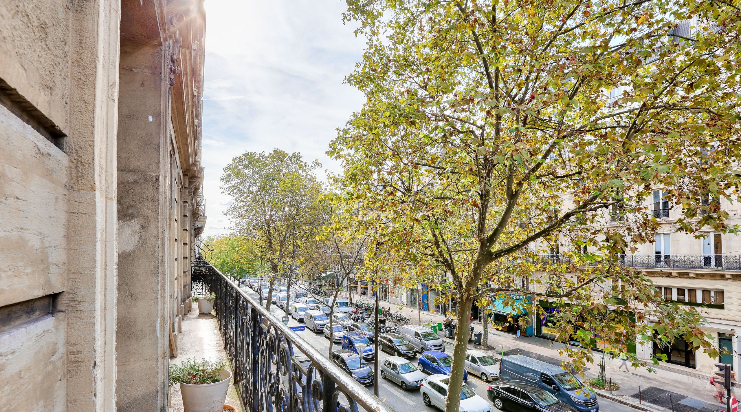 Un balcon agrémenté d’un pot de fleurs, donnant sur une rue animée, avec des voitures et des immeubles.