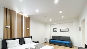 A modern hotel room with a bed, a sofa, and a wall-mounted panel. - Urban Flat 52 - Charming Cosy Flat in Center of Paris (París)