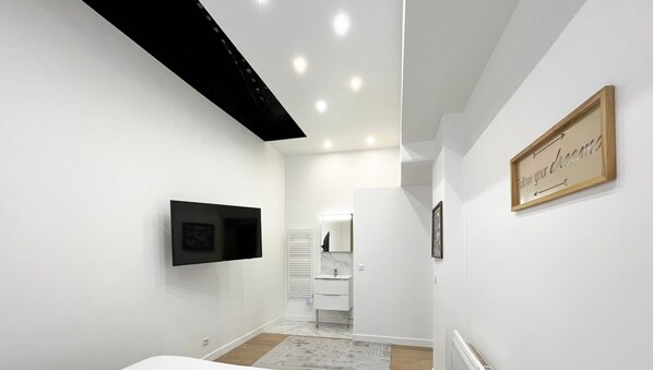A modern, well-lit hallway with a flat-screen TV mounted on the wall, a wooden-framed sign on the right, and a glimpse of a bathroom in the background. - Urban Flat 52 - Charming Cosy Flat in Center of Paris (París)