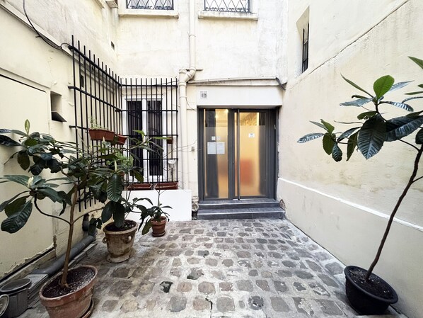 A narrow alleyway with a door, potted plants, and a stone-tiled floor.