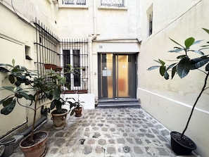 A narrow alleyway with a door, potted plants, and a stone-tiled floor. - Urban Flat 52 - Charming Cosy Flat in Center of Paris (París)