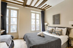 Habitación de hotel con dos camas, ventanas amplias con cortinas, techo de madera y un cuadro en la pared.