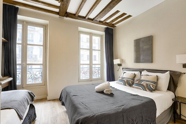 Habitación de hotel con dos camas, ventanas amplias con cortinas, techo de madera y un cuadro en la pared.