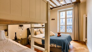 A bedroom with a bunk bed, a single bed, a window with a view, and a teddy bear on the single bed.
