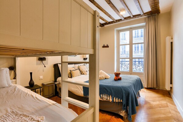 A bedroom with a bunk bed, a single bed, a window with a view, and a teddy bear on the single bed.