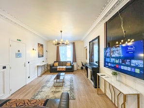 A hotel lobby with a sofa, a TV displaying Disney+ channels, and a chandelier.