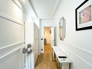 A hallway with a white fan, a framed picture, and a table with a remote control.