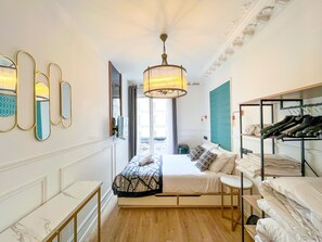 A hotel room with a bed, a wardrobe, a mirror, a chandelier, and a window with curtains.