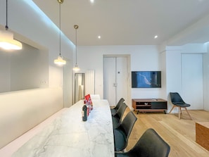 A modern living room with a marble dining table, black chairs, a flat-screen TV, and pendant lighting. - Urban Flat 69 - Beautiful Parisian Apartment in Center of Paris (París)