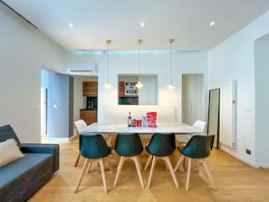 A modern kitchen with a dining table, four chairs, pendant lights, and a refrigerator. - Urban Flat 69 - Beautiful Parisian Apartment in Center of Paris (París)