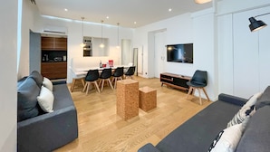 A modern living room with a sofa, a dining area with chairs, a coffee table, a TV, and a lamp. - Urban Flat 69 - Beautiful Parisian Apartment in Center of Paris (París)
