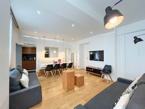 Ett modernt vardagsrum med en soffa, en matplats med stolar, ett soffbord, en tv och en lampa.