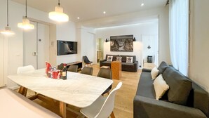 A modern living room with a dining area, a sofa, a TV, and artwork on the walls. - Urban Flat 69 - Beautiful Parisian Apartment in Center of Paris (París)