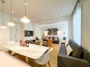 Ett modernt vardagsrum med en matplats, en soffa, en tv och konstverk på väggarna.