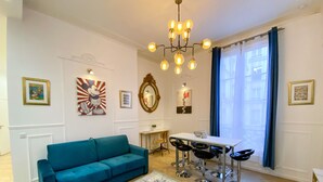Ein Wohnzimmer mit einem Türkis-farbenen Sofa, einem Esstisch mit Barhocker, einer Kandelaber und Wandbildern.