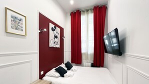 Ein Hotelzimmer mit einem Bett, einem an der Wand montierten Flachbildfernseher, einem gerahmten Bild und roten Vorhängen.