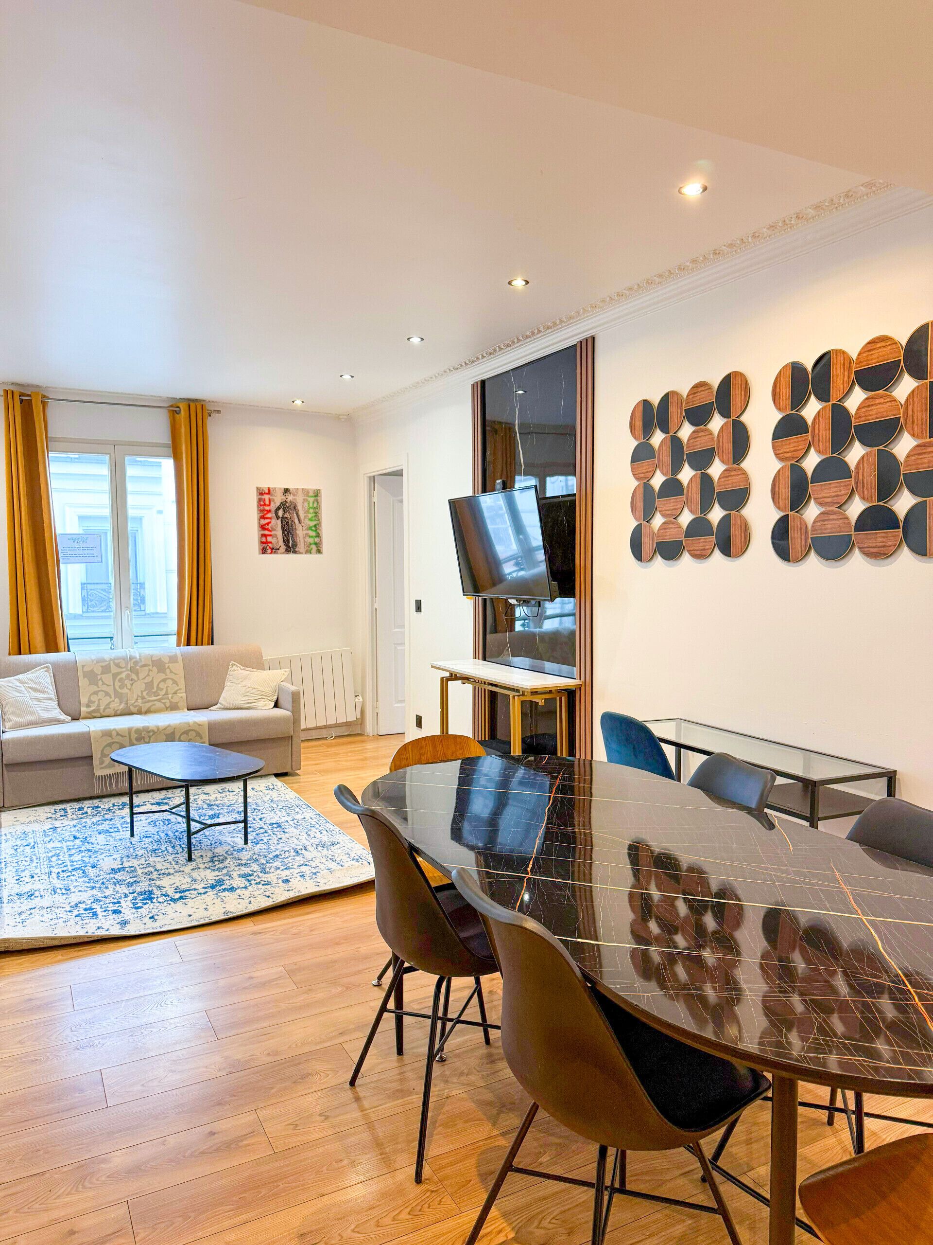 Una sala de estar moderna con una mesa de comedor de vidrio, asientos cómodos, un sofá y un adorno en la pared.