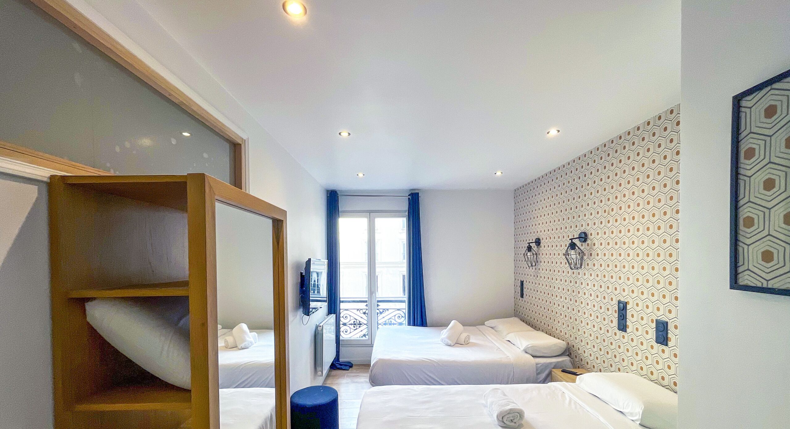 Ett hotellrum med två sängar, en trägarderob, en liten pall och en vägg med mönster.
