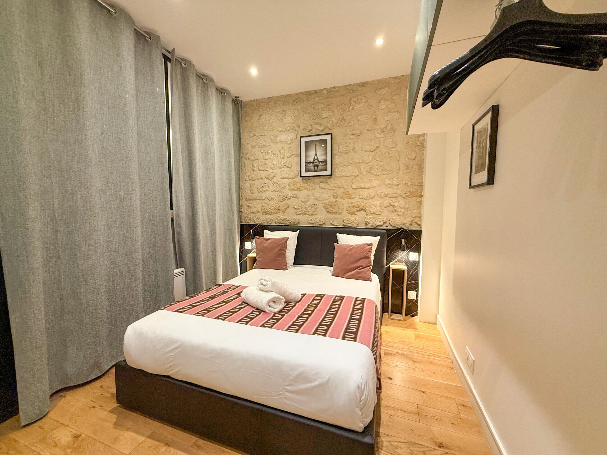 A hotel room with a large bed, a stone wall, and a picture of the Eiffel Tower.