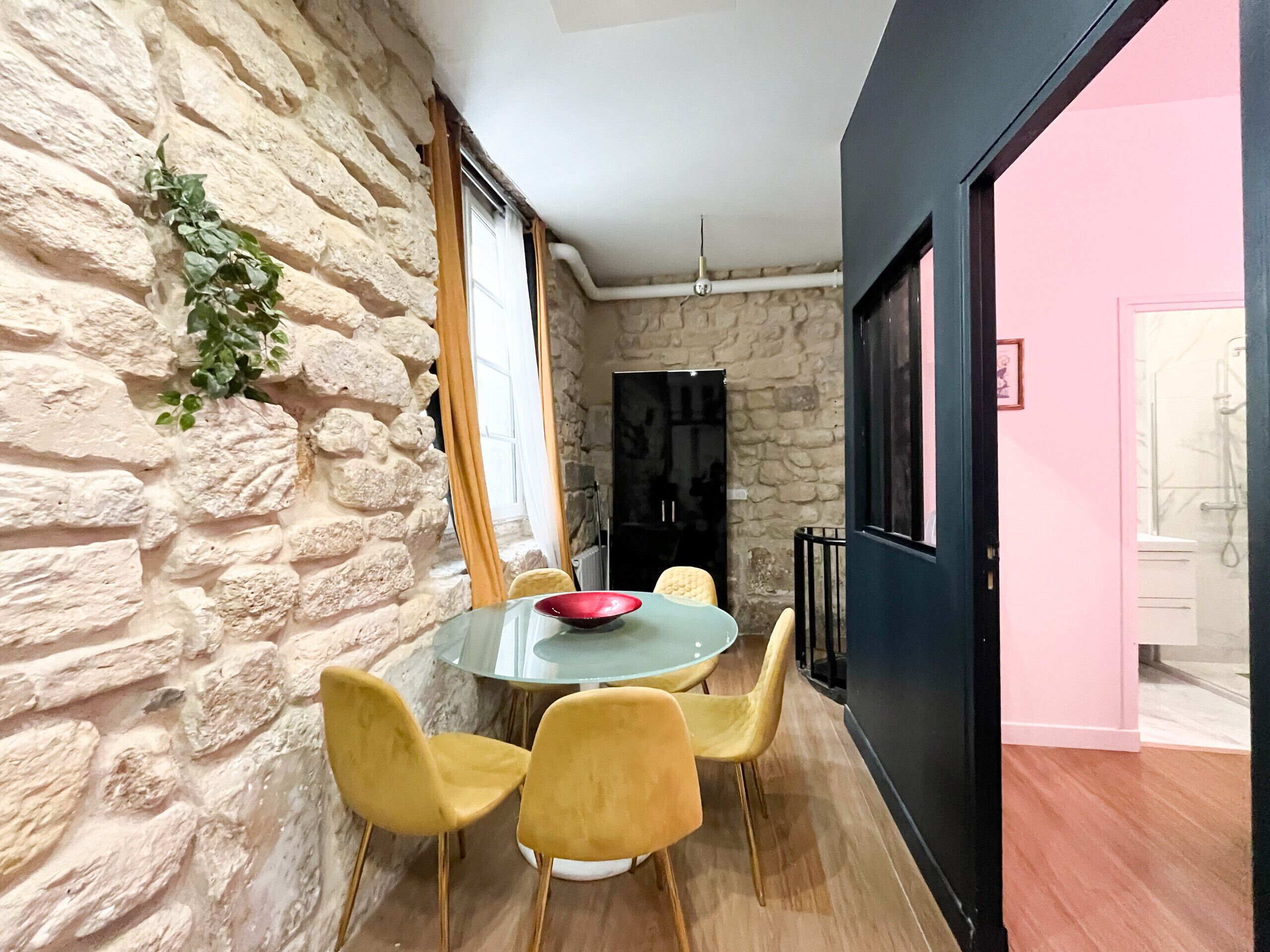 A dining area with a stone wall, a round table, yellow chairs, and a red bowl.
