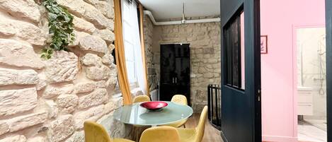 A dining area with a stone wall, a round table, yellow chairs, and a red bowl.