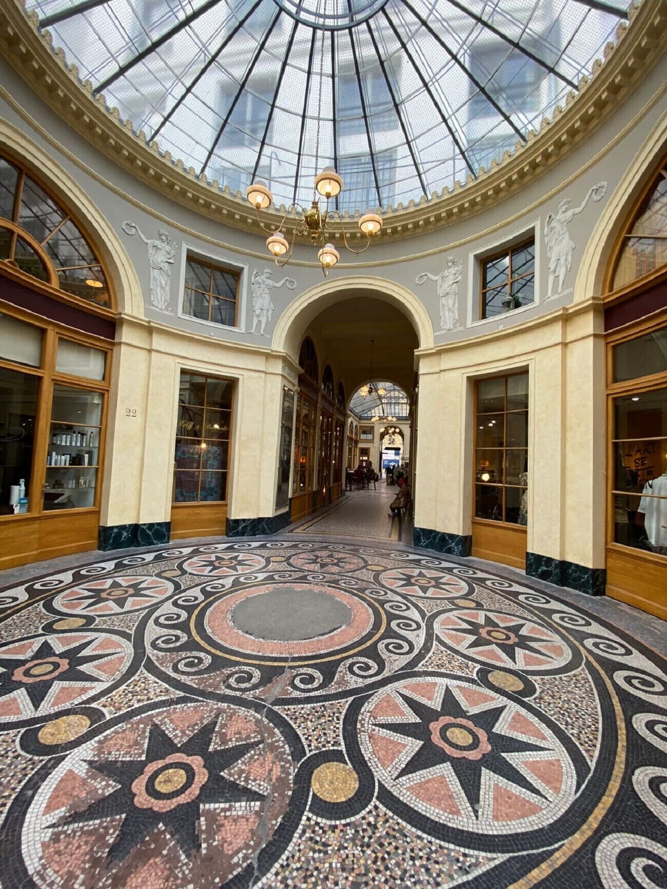 En storslagen hall med ett högt glastak, utsmyckade pelare och ett detaljrikt mosaikgolv.