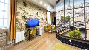 A modern living room with a stone wall, a flat-screen TV, a dining area with yellow chairs, and a large window with a cityscape view. - Urban Flat 154 - Pretty 2 BDR in center of Paris (París)