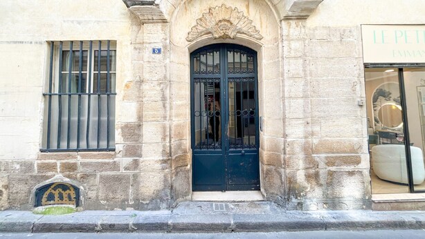 A building with a stone facade, a black ornate door, and a window with metal bars. - Urban Flat 154 - Pretty 2 BDR in center of Paris (París)