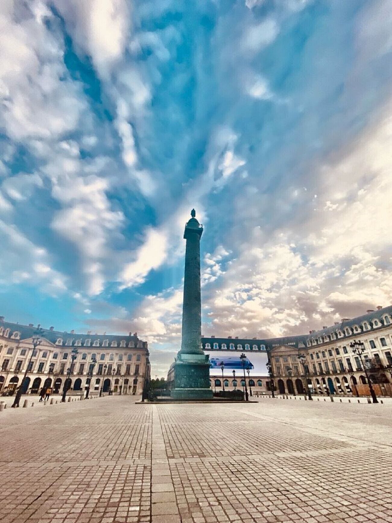 A large open plaza with a tall monument in the center, surrounded by classical architecture.