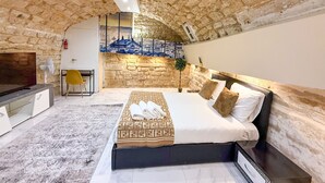 A bedroom with a stone wall, a bed with a patterned bedspread, a TV, and a small table with a chair. - Urban Flat 154 - Pretty 2 BDR in center of Paris (París)