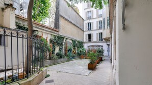 A narrow courtyard with a tiled floor, potted plants, and a wrought iron fence.