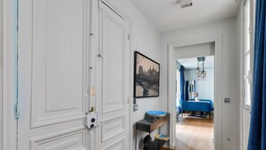 A hallway with a white door, a framed picture, and a blue dining area in the background.