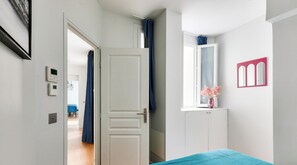 Ein Zimmer mit einer weißen Tür, einem Fenster mit pinkfarbenem Rahmen und einem Bett mit blauer Decke.