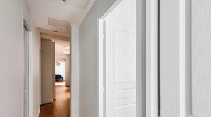 Un pasillo con puertas blancas, una zona de comedor con una mesa y sillas azules, e iluminación empotrada en el techo.