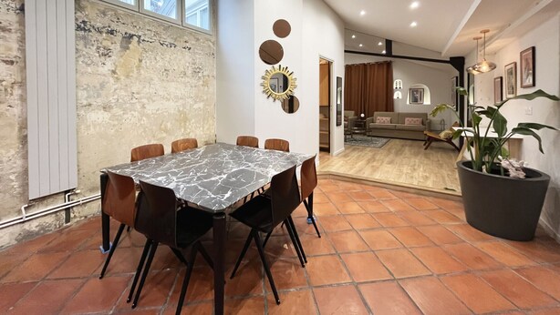 A dining area with a marble table and chairs, a rustic brick wall, and a view into the living room. - Urban Flat 161 - Sublime 4BDR Luxury Flat in Paris (París)