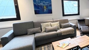 A modern living room with a grey sectional sofa, a wooden coffee table, and a large window with blinds. - Urban Flat 166 - 4BDR Luxury Apartment in Center of Paris (París)