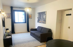Una sala de estar moderna con un sofá gris, una mesa redonda negra, un tapete estampado, un globo terráqueo sobre una mesita auxiliar y una pintura de un paisaje urbano en la pared.