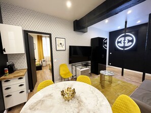 En moderne stue med et marmorbord, gule stole, et fjernsyn og et sort skab med et Chanel logo.