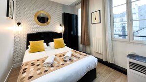 Ein Hotelzimmer mit einem Bett, einem runden Spiegel, einem Heizkörper und einem Fenster mit Vorhängen.