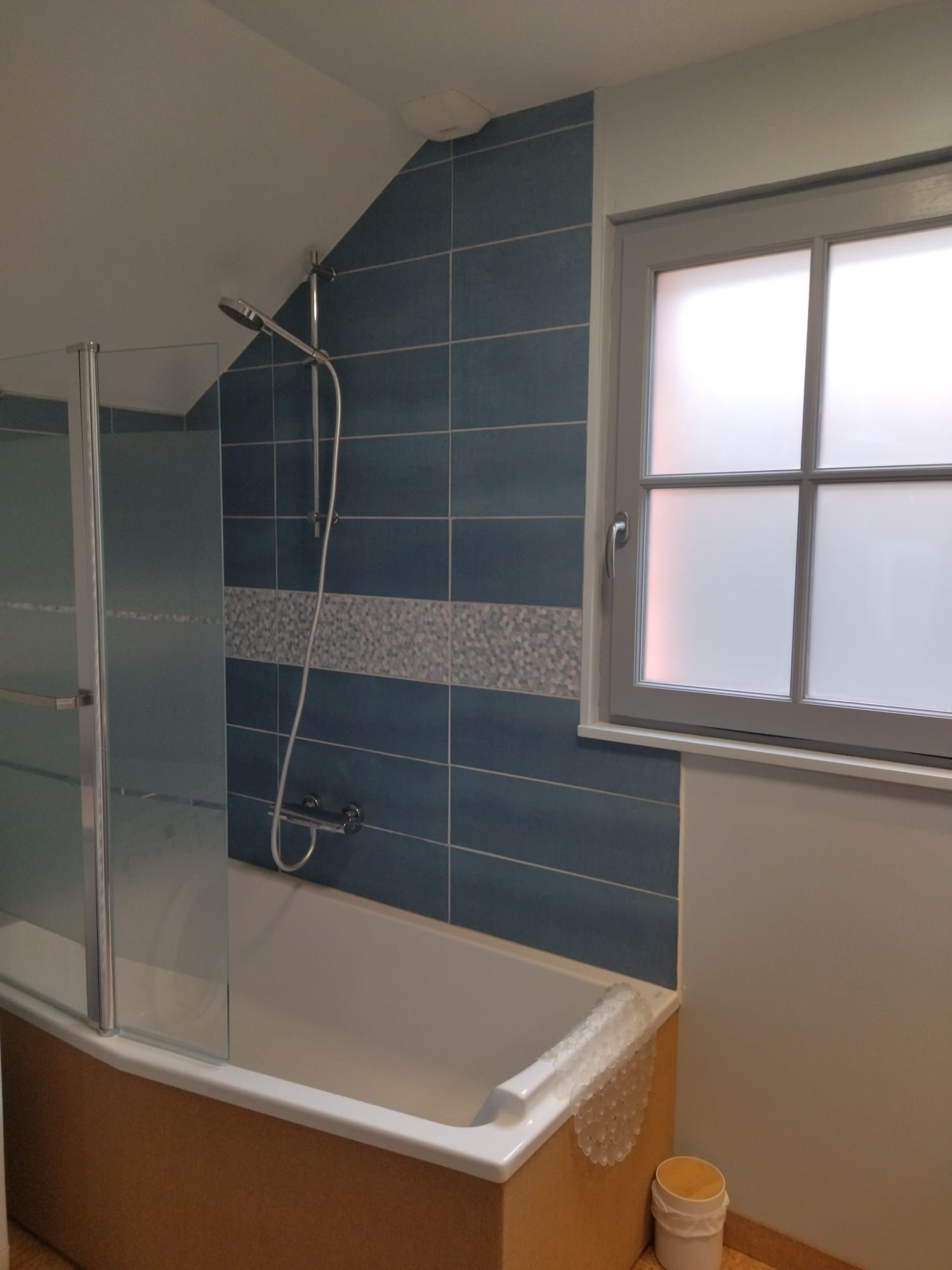 Ein Badezimmer mit einer Duschkabine aus Glas, einer Badewanne und einem Fenster mit satinierten Scheiben.