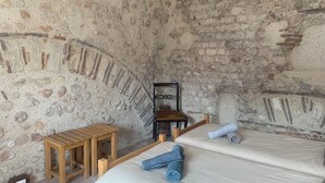 Una stanza con una parete in pietra, un letto di legno, un tavolino in legno e una sedia.