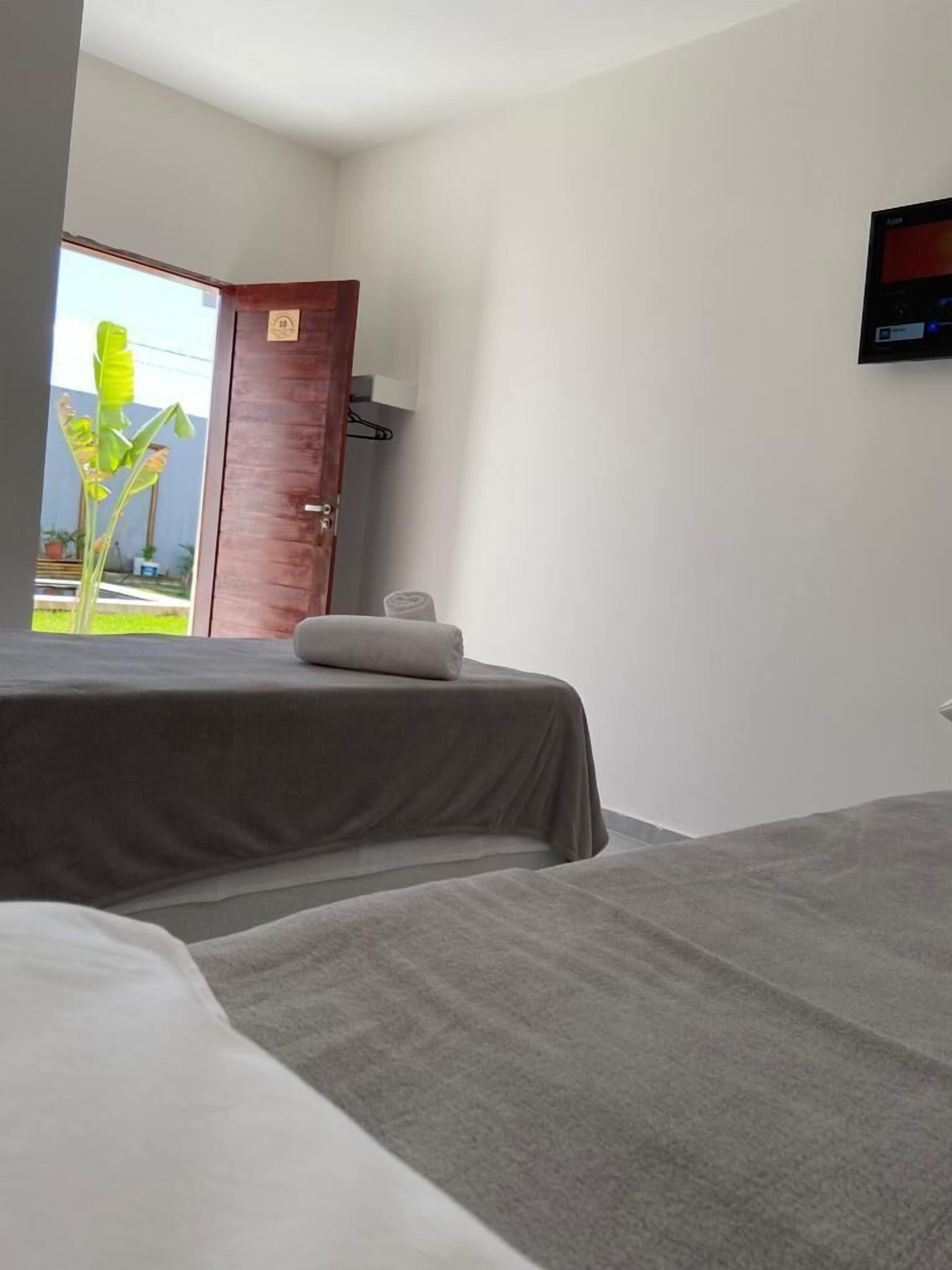 A hotel room with a bed, a TV mounted on the wall, and a door leading to a balcony with a view of greenery.