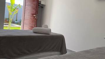 Ein Hotelzimmer mit Bett, einem an der Wand befestigten Fernseher und einer Tür zu einem Balkon mit Blick auf Grünflächen.