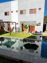 Un edificio moderno con piscina, hamaca y mobiliario para exteriores.