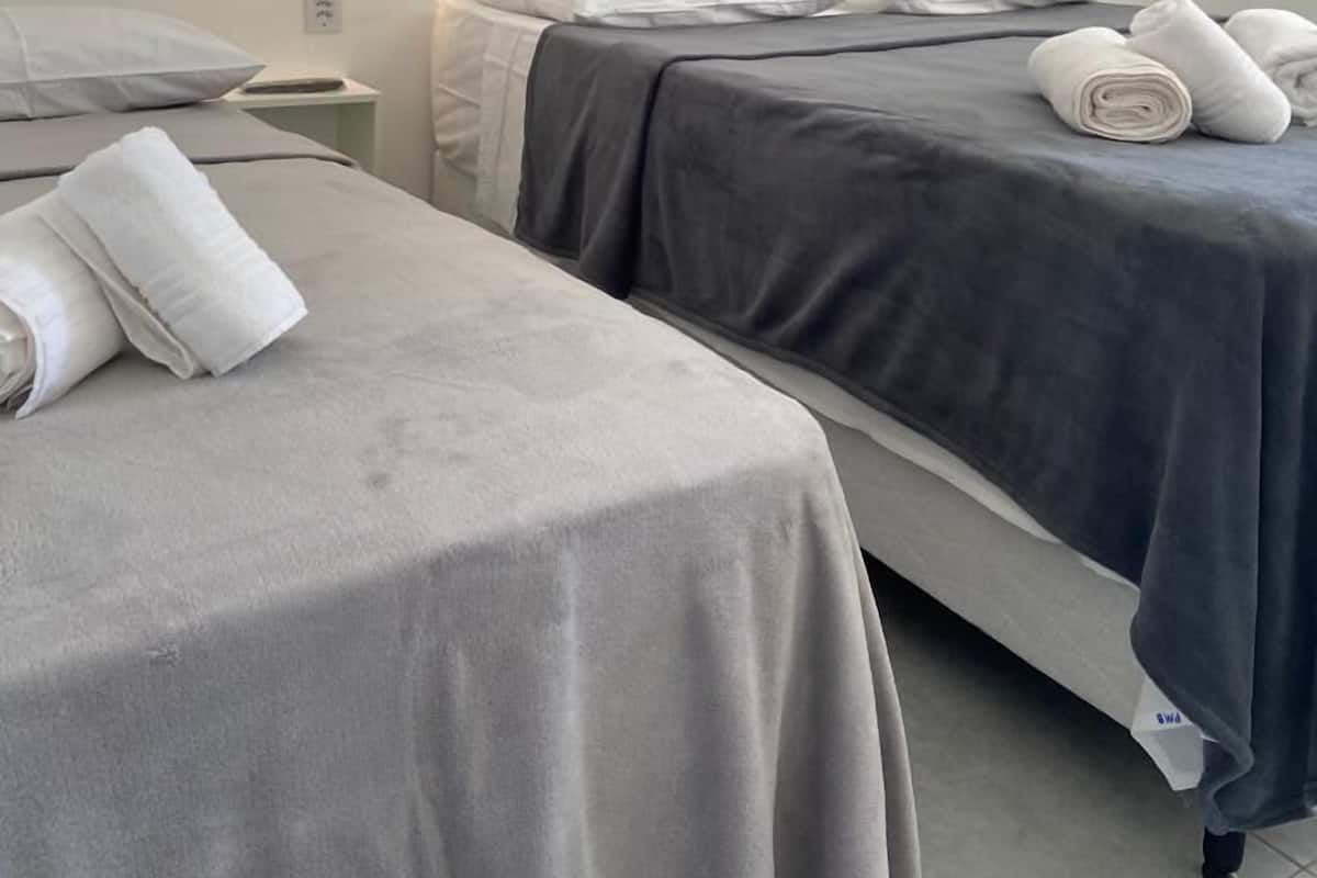 Ein Hotelzimmer mit zwei Betten, jeweils mit grauer Bettdecke und weißen Kissen. Darüber an der Wand hängen drei gerahmte Bilder.