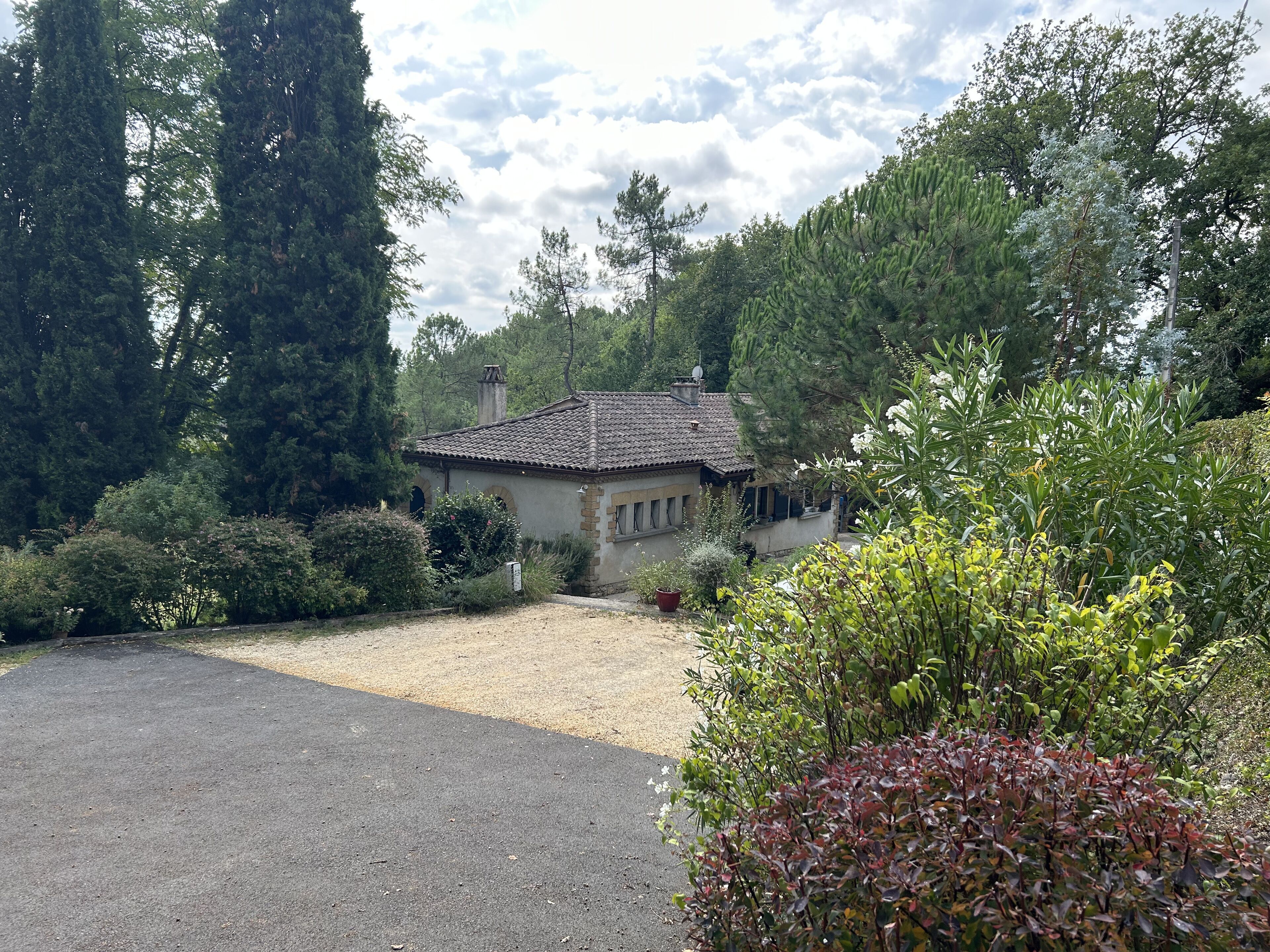 Une maison avec un toit en tuiles, entourée d’une végétation luxuriante et d’arbres.